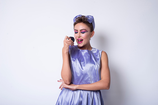 Girl in purple dress eating a plum and she grimaces. Fashion Photography.