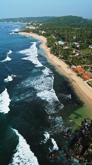 La vista aérea revela las aguas turquesas de la playa de Dalawella, las palmeras que se balancean y las arenas doradas de Sri Lanka. Los vacacionistas disfrutan de la laguna tropical, nadan en aguas cristalinas, se relajan en la costa serena. photo