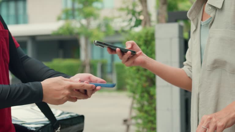 Closeup of Consumer paying using smartphone and NFC technology to courier for package delivery at home. Food delivery service.