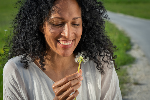 Front view of mature woman blowing dandelion seeds in meadow.