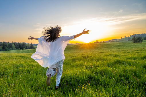 Rear view of mature woman walking with arms outstretched in meadow.