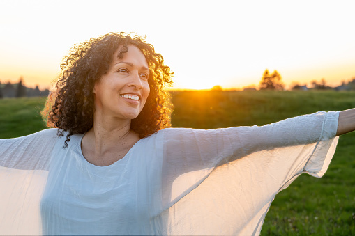 Smiling mature woman walking with arms outstretched in meadow.