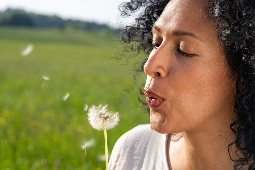 Mature woman blowing dandelion seeds in meadow.