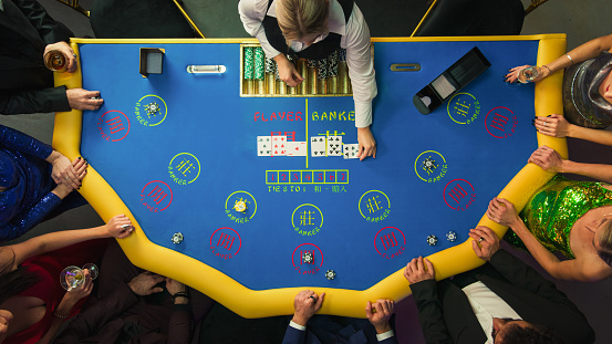 Top Down View Of Glamorous Casino Gamblers Placing Bets and Having Fun While Winning at Baccarat Table. Professional Croupier Dealing Cards, VIP People Enjoying Luxurious Lifestyle, Feeling Lucky.