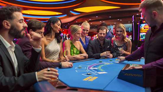 Diverse Group of Glamorous People Playing Game of Blackjack at Stylish Casino. Patrons Having Good time Luxury Evening on Casino Floor, Placing Betts, Sociolizing. Triumphant Gorgeous Lady Wins