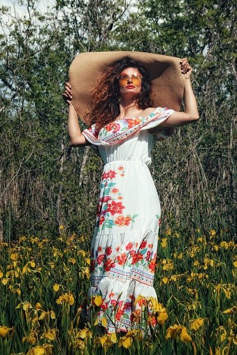 Lady in floral dress wearing big hat standing in a flower field