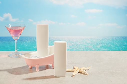 Front view of unlabeled white bottle arranged with pink bathtub, a starfish and cocktail glass with pink beverage. Skin care cosmetic product mockup with empty label