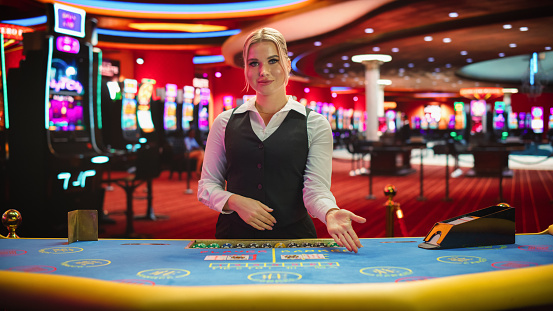 Professional Female Croupier in Casino Dealing Playing Cards on a Baccarat Table. Beautiful Dealer of a Live Online Casino Reveals Winning Results of the Card Game Bets, Looking at the Camera