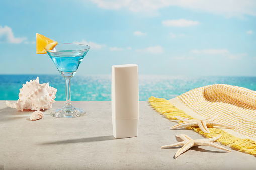 White tube without label placed on a concrete surface near the pool with conch shells, starfishes, cocktail glass and a scarf. Natural cosmetic concept. Empty label for branding mockup