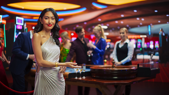 Portrait of a Beautiful Young Asian Woman Wearing an Elegant Silver Dress, Standing in a Modeling Pose and Gesturing at an Empty Space for Your Company Logo or Advertising Campaign Call to Action