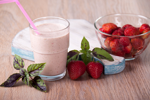 Smoothies with strawberries and basil in a glass and strawberries and basil leaves on a table