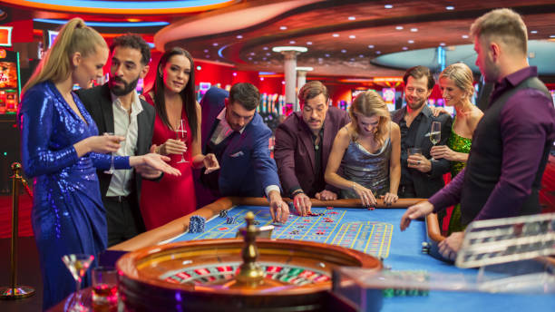 gathering of wealthy young individuals, standing together around a roulette table in a contemporary casino setting. cinematic nightlife footage, carefree gamblers congratulating the winning players - gamblers foto e immagini stock