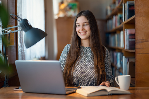 Cheerful female student in university library, preparing assignment