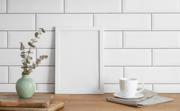 istock A  frame with a blank canvas against a white tile wall and on a wooden tabletop with vase and cup of tea. 1924464001