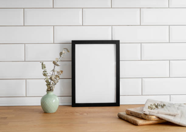 istock A black frame with a blank canvas against a white tile wall and on a wooden tabletop 1924464007