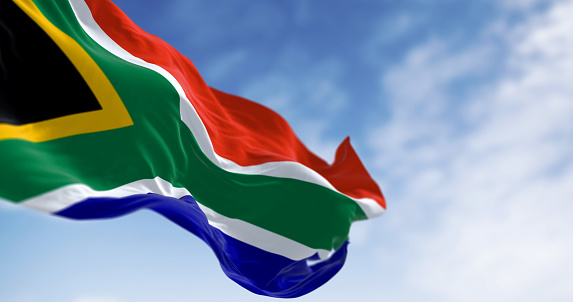 Detail of the South Africa flag waving. Red and blue flag divided by a green Y that encloses a black triangle with a yellow border. 3d illustration render. Selective focus. Close-up.