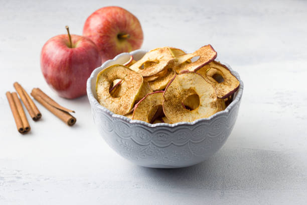 Homemade dried apples with cinnamon, apple chips in a bowl with cinnamon sticks on a light gray background. Delicious healthy snack.