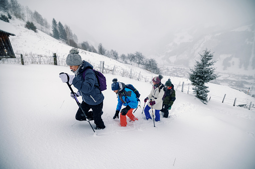Mother and three kids are hiking in European Alps on a winter day. Family is walking up in the deep snow.\nSnowy overcast winter day.\nShot with Canon R5