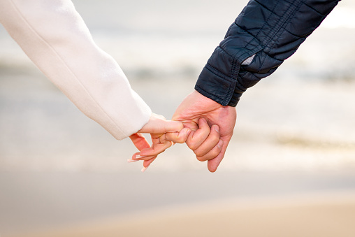 Young couple in love, Attractive man and woman enjoying romantic evening on the beach, Holding hands watching the sunset.Closeup.
