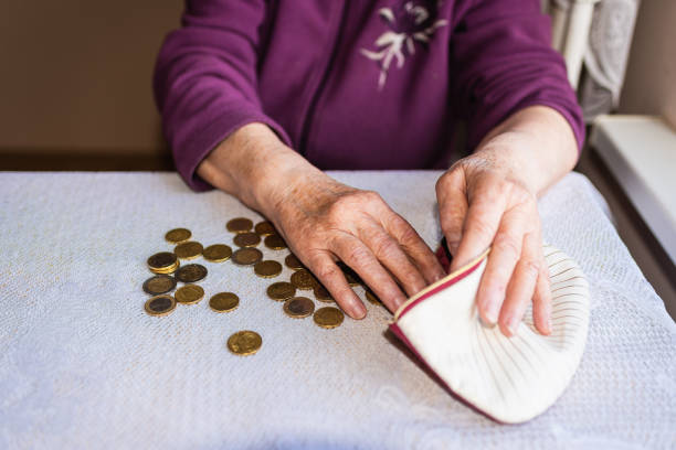 Old woman sitting miserably at home and counting remaining coins from the pension in her wallet after paying the bills. Concerned elderly woman sitting at home and counting remaining coins.old woman sitting miserably at the table at home and counting remaining coins from the pension in her wallet after paying the bills ira gold custodians stock pictures, royalty-free photos & images