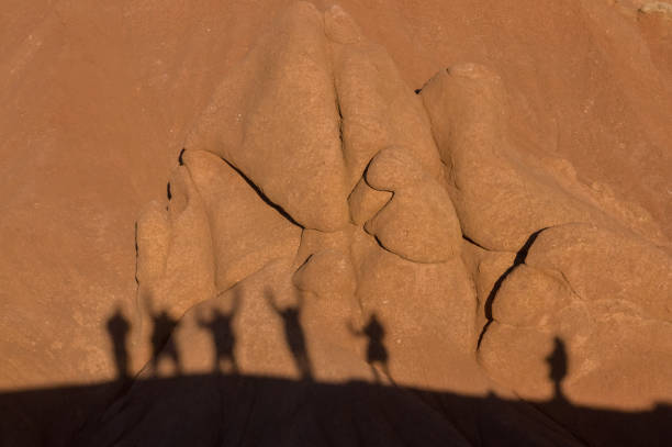 The elongated shadows of tourists traverse the undulating canyon walls, a stark contrast of human vivacity against the still, enduring formations sculpted by the relentless forces of nature over time.