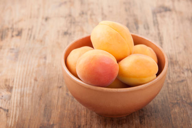 Apricots in a clay bowl on a wooden table stock photo