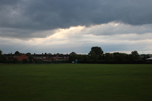 Open green playing field with residential houses in background and cloudy sky