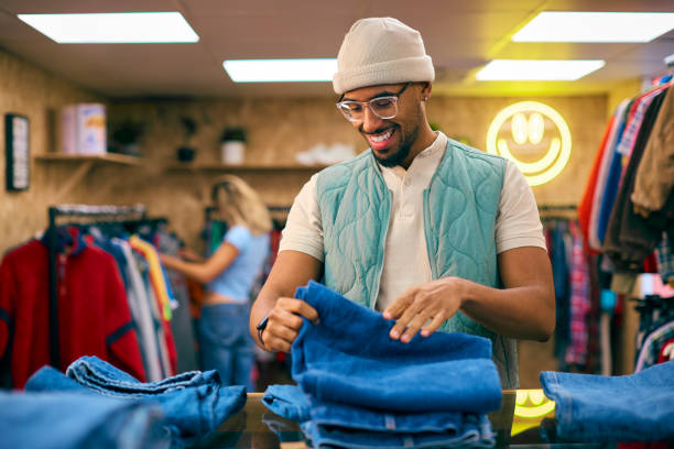 männlicher verkaufsassistent oder kunde, der jeans im modegeschäft sortiert und anschaut - tragen stock-fotos und bilder