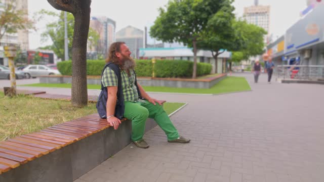 Long-haired elderly man with a beard sitting on a bench in the city