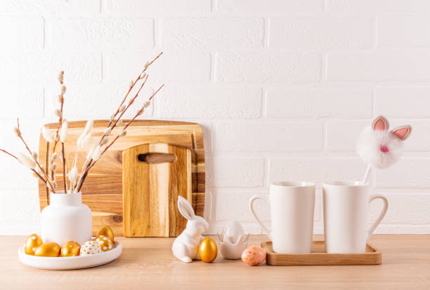 istock Kitchen festive background for Easter holiday. Easter golden eggs, ceramic bunnies, kitchen utensils and two white mugs. Front view. Light colors. 1924552754