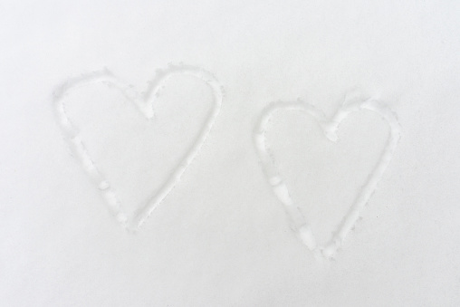 Two drawn hearts in the snow, top view