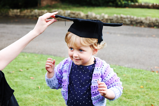 Young mum playfully putting her mortarboard hat on her young daughter after she received her masters degree.