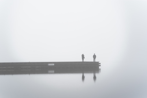 Two people on a dock in thick fog at Beach Park, Orillia, Ontario, Canada