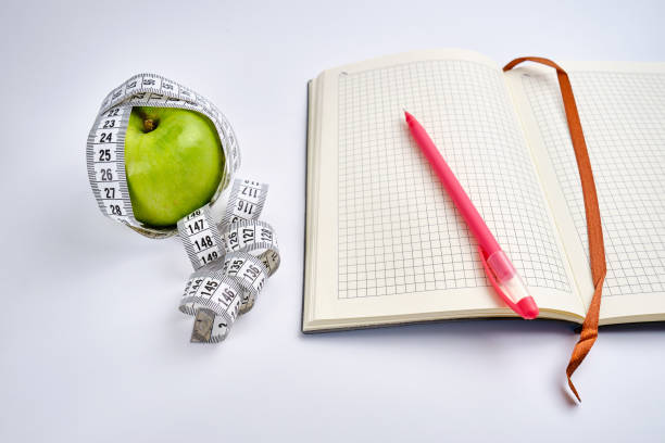 istock White centimeter, open notepad and green apple on a colored background. Healthy eating, calorie content. Nutrition, figure and health concept 1924629650