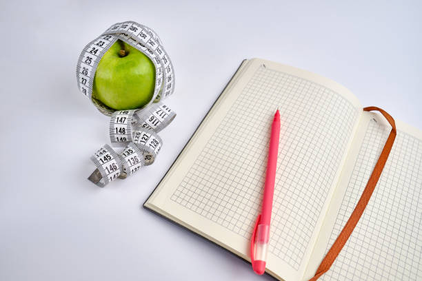 istock White centimeter, open notepad and green apple on a colored background. Healthy eating, calorie content. Nutrition, figure and health concept 1924633408