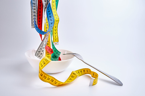 Fork, plate and measure tape on white background. Diet and obesity concept.