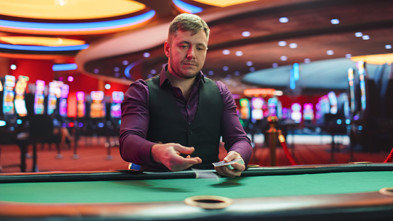 Caucasian Male Poker Dealer Is Dealing Playing Cards In Luxurious Casino. Experienced Croupier Setting Up New Game For Professional High Stakes Gamblers To Make Bets, Bluff, And Win Big Money.