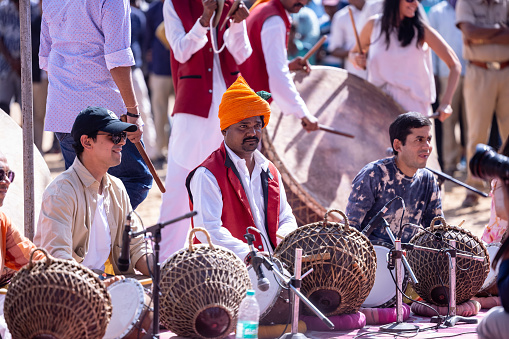 Pushkar, Rajasthan, India - November 2022: Unidentified tourists playing drums in colorful clothes at fair ground during the pushkar camel fair.