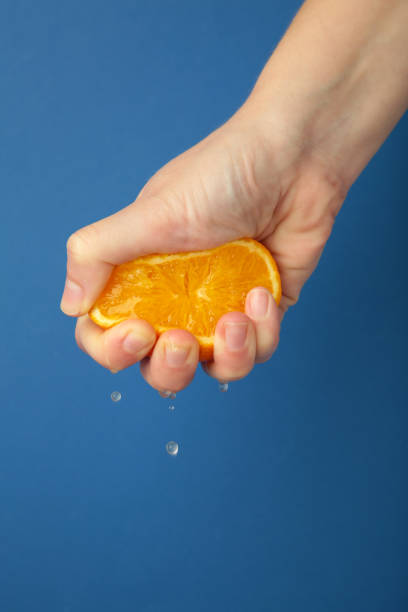 istock Female hand squeezing half of orange on blue background. 1924716397