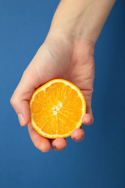 istock Female hand squeezing half of orange on blue background. Vertical photo 1924716408