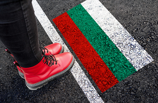 a woman with a boots standing on asphalt next to flag of Bulgaria and border
