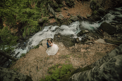 Wedding couple is hugging near the mountain river. Groom and bride . Nature wedding photoshoot. Photo session in the forest of the bride and groom.