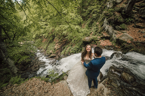 Happy wedding couple on the edge of a waterfall. Groom and bride. Wedding photo session in nature. Photo session in the forest of the bride and groom.