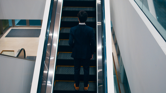 Smart young Asian businessman CEO wearing business suit going up on escalator at business center and standing in modern office, Professional executive manager working at modern office building, Business people at work