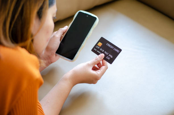 istock Asian woman holding black credit card lying on sofa 1924766982