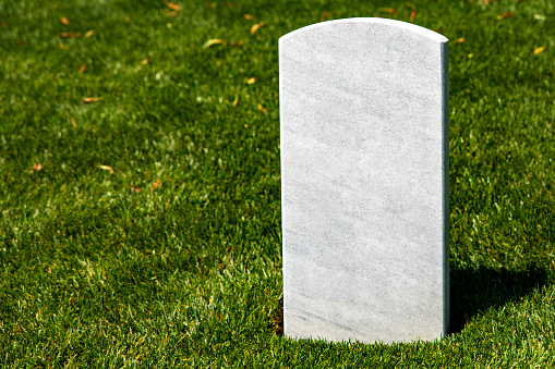 A white marble tombstone on a grassy lawn at Arlington National Cemetery, a military cemetery in Washington DC, the capital of the USA.
