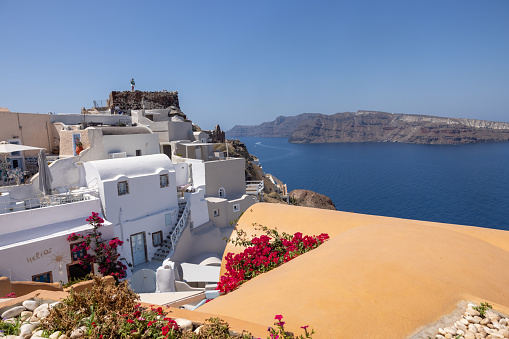 Oia, Santorini, Greece - July 3, 2021: Whitewashed buildings and the ruins of Castle of Agios Nikolaos on the edge of the caldera cliff, Oia village, Santorini, Greece