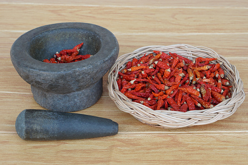 Old granite stone mortar with pestle and basket of red dried chillies for cooking.Concept, kitchen utensils .Thai cooking tool, use to pound chili paste or curry paste.