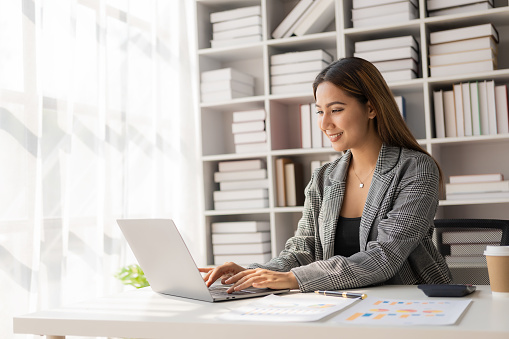 Asian businesswoman working at home office and analyzing financial documents and calculator, phone, laptop on table, financial report concept. business plan investment