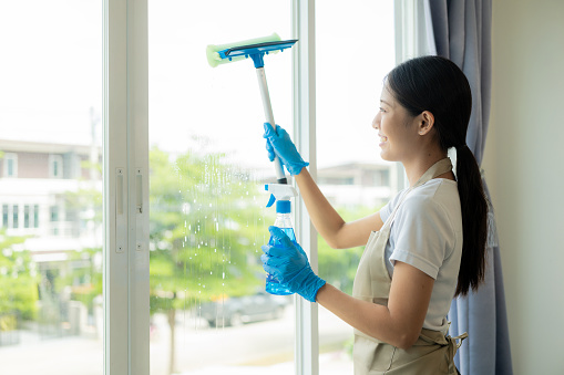 Beautiful Asian housewife doing housework and cleaning the house with an apron, using a vacuum cleaner, mop, cloth to clean the floor in the living room. Happy housewife doing housework